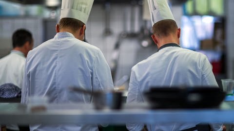 Zwei Auszubildende mit Kochmützen sind von hinten zu sehen (Foto: dpa Bildfunk, Picture Alliance)