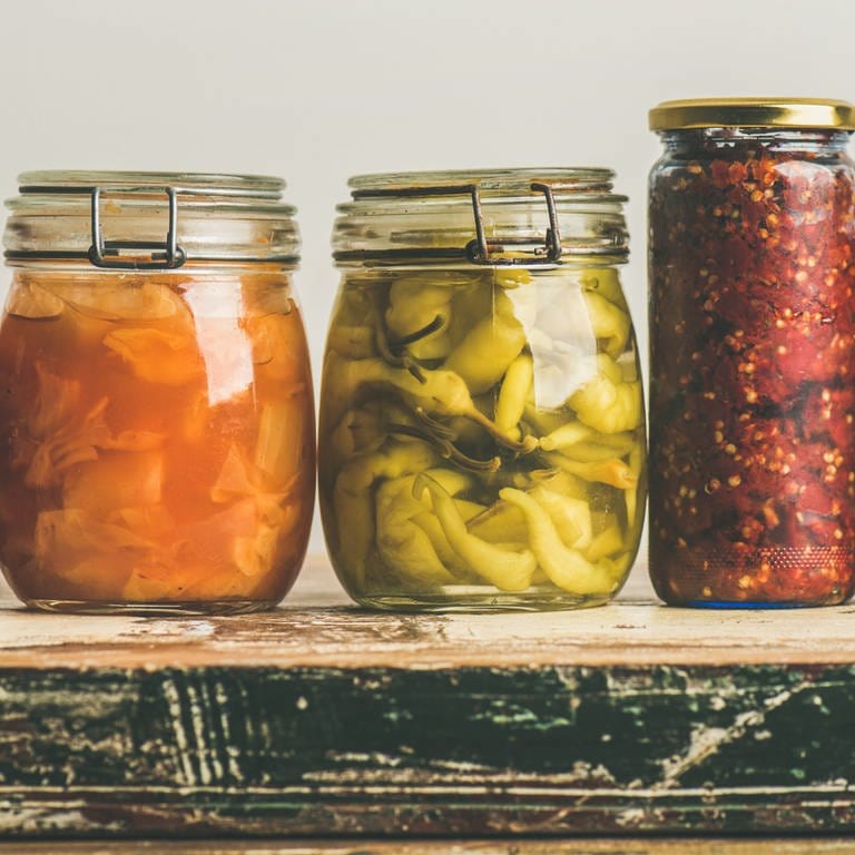 Verschiedene Gläser mit fermentiertem Gemüse stehen auf einem Tisch.