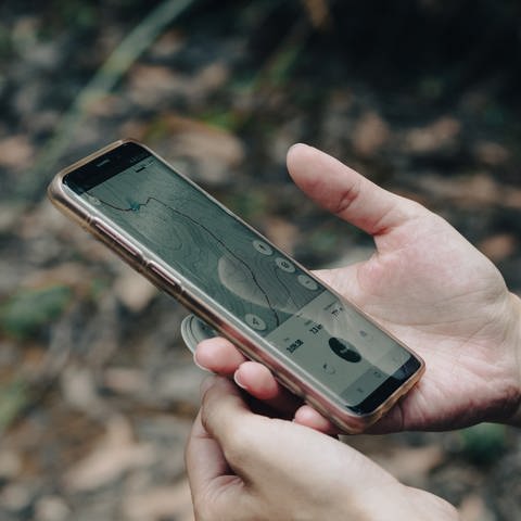 Nahaufnahme von Händen die ein Smartphone mit geöffneter Wander-App halten. Wander-Apps: Worauf sollte man achten? (Foto: Unsplash / Iliya Jokic)