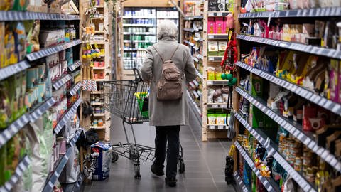 Ältere Frau von hinten gesehen schiebt einen Einkaufswagen an Supermarkt-Regalen vorbei. Preissteigerungen: Lebensmittel werden teurer (Foto: dpa Bildfunk, picture alliance/dpa | Sven Hoppe)
