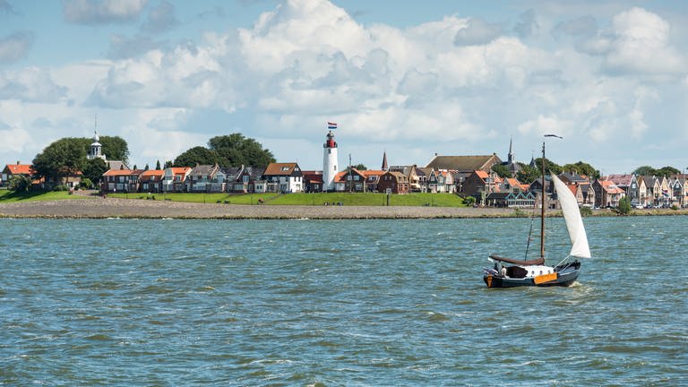 Vom Ijsselmeer aus blickt man auf ein niederländisches Dorf an der Küste mit Leuchtturm und einem Schiff auf dem Wasser.  (Foto: Colourbox)