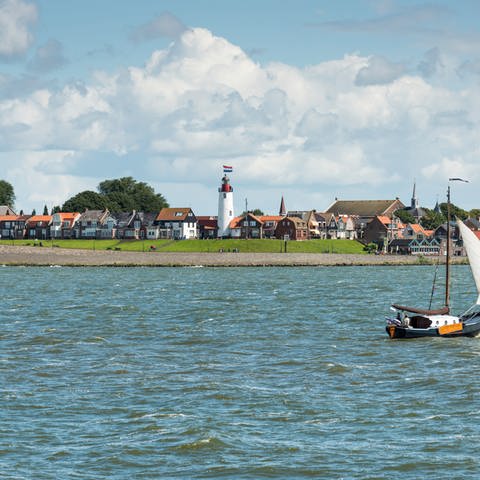 Vom Ijsselmeer aus blickt man auf ein niederländisches Dorf an der Küste mit Leuchtturm und einem Schiff auf dem Wasser.  (Foto: Colourbox)