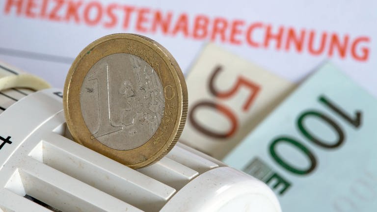 ILLUSTRATION - Eine Euromünze steckt in einem Heizungsthermostat, der auf Heizkostenabrechnungen und Euro-Geldscheinen liegt.  (Foto: dpa Bildfunk, picture alliance/dpa | Jens Büttner)