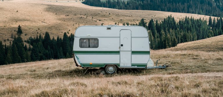 Ein kleiner Caravan mit dunkelgrünem Streifen steht inmitten einer Landschaft.  (Foto: Unsplash/Leo Foureaux)