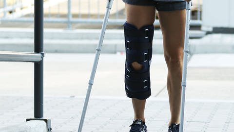 Junge Frau mit Beinschiene und Krücken - nur die Beine sind zu sehen. Wird das Knie falsch belastet, kann das Kreuzband reißen. (Foto: dpa Bildfunk, Picture Alliance)