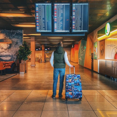 "Probleme im Urlaub - Geld zurück nach Reise-Chaos"   steht im Vordergrund auf einem semitranspartenen grünen Hintergrund. Im Hintergrund ist ein Mann mit seinem Koffer vor einer Anzeigetafel am Flughafen.  In der rechten oberen Ecke ist die Bildquelle vermerkt. (Foto: Unsplash / Danila Hamsterman)