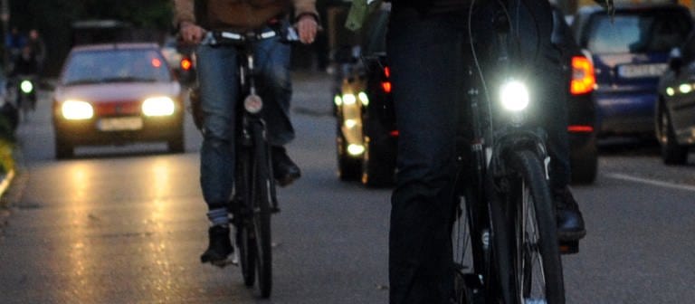Ein Fahrrad mit Beleuchtung und eines ohne Licht fahren im Dunkeln nebeneinander (Foto: dpa Bildfunk, Picture Alliance)