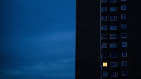 In einem Hochhaus vor dunklem Himmel ist nur ein Fenster beleuchtet. Die Preisbremse bei Strom und Gas soll Verbraucher entlasten. Wie kann man Geld sparen? (Foto: dpa Bildfunk, picture alliance/dpa | Julian Stratenschulte)