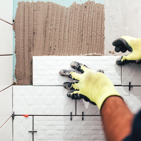 Ein Handwerker befestigt Badfliesen an einer Wand. (Foto: Adobe Stock)