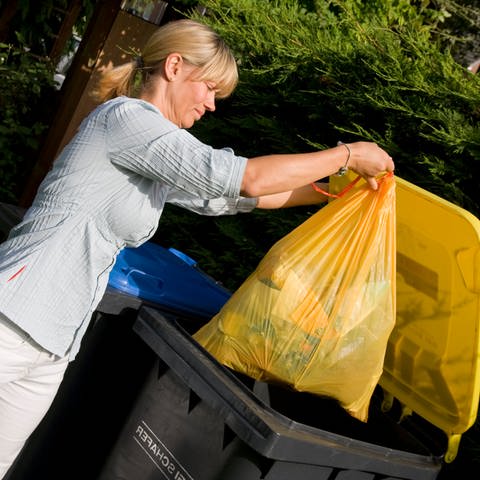 Blonde Frau wirft gelben Müllsack in eine schwarze Mülltonne mit gelbem Deckel. Müllbeutel von Profissimo dm, Gut und Günstig, Swirl, Pely im Test: Welche sind stabil und reißfest? (Foto: Colourbox)