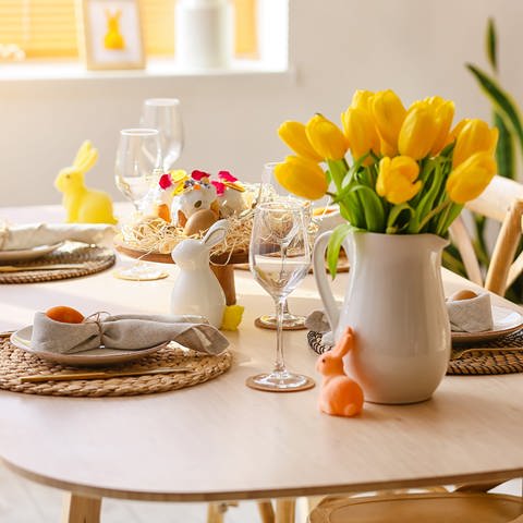 Österlich gedeckter Tisch mit Osterhasenfiguren und gelben Tulpen. Aldi oder Lidl: Wer hat die besten Gourmet- und Deluxe-Produkte für's Ostermenü? (Foto: Adobe Stock)