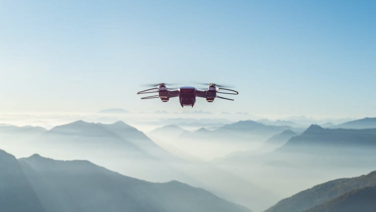 Drohne fliegt über Bergpanorama. Wie viel sollte eine vernünftige Drohne kosten und wer darf sie fliegen? (Foto: Unsplash/Alessio Soggetti)