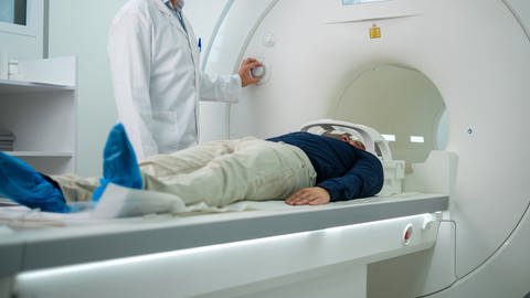 Ein Arzt in weißem Kittel fährt einen Patienten auf einer Liege in die runde MRT Röhre. (Foto: Adobe Stock)