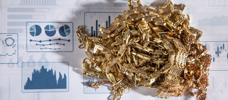 Der Goldkurs ist hoch, viele wollen ihr Gold zum Beispiel in Form von Schmuck verkaufen. Aber Vorsicht: Zahlreiche Goldhändler machen unfaire Angebote. Goldschmuck liegt auf einem Papier mit Statistiken. (Foto: Colourbox)