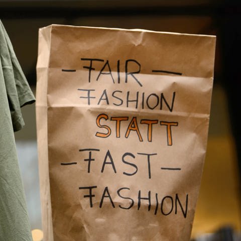 Demonstranten halten in Stuttgart ein T-Shirt mit der Aufschrift "Mir ist nicht egal wer dieses T-Shirt gemacht hat" und eine Tüte mit der Aufschrift "Fair Fashion statt Fast Fashion" hoch. (Foto: dpa Bildfunk, picture alliance/Sina Schuldt/dpa)