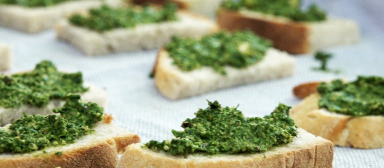 Mit grünem Pesto bestrichene Weißbrot-Scheiben liegen nebeneinander auf einer Platte. Rezept für Pesto aus Karottengrün, Radieschenblättern und Kohlrabiblättern. (Foto: SWR)