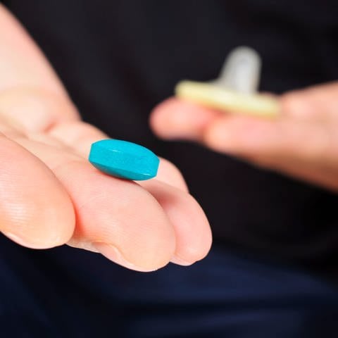 Auf einer Hand liegt eine blaue Viagra Pille, die gegen Erektionsprobleme helfen soll. Im HIntergrund ist ein Kondom zu sehen. (Foto: Colourbox/nito)
