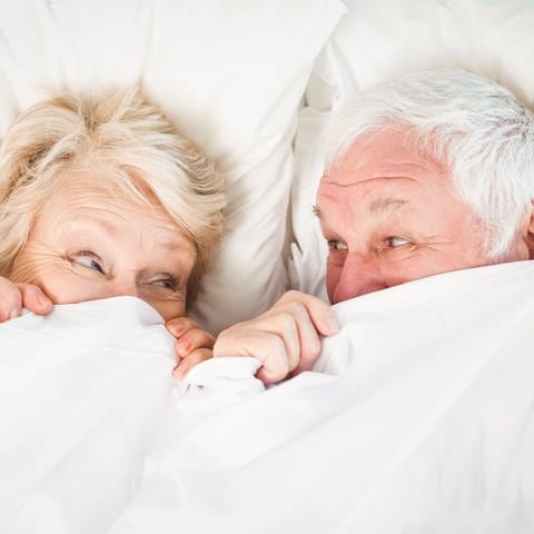 Ein Ehepaar etwa Mitte Siebzig liegt glücklich im Bett und hat die Decke bis zur Nase hochgezogen: Sie haben ihr Probleme beim Sex überwunden. (Foto: Adobe Stock)