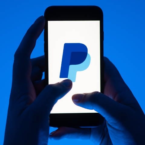 Zwei Hände halten Smartphone, auf dem das Paypal-Logo zu sehen ist. Wie Betrüger den Käuferschutz aushebeln - eine neue Betrugsmasche. (Foto: dpa Bildfunk, Sebastian Kuhnert)