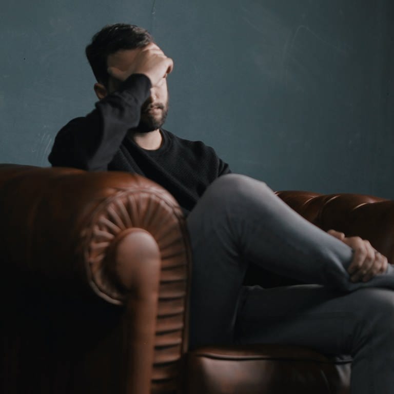 Mann sitzt niedergeschlagen mit Hand vor dem Gesicht auf einem Ledersofa. Wie stellt man sicher, dass die Berufsunfähigkeitsversicherung im Ernsfall greift? (Foto: Unsplash/Nik Shuliahin)