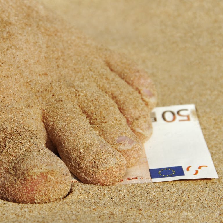 Fuß steht im Sand auf einen 50-Euroschein. Auslandskrankenversicherung: Worauf sollte man achten? (Foto: Colourbox)