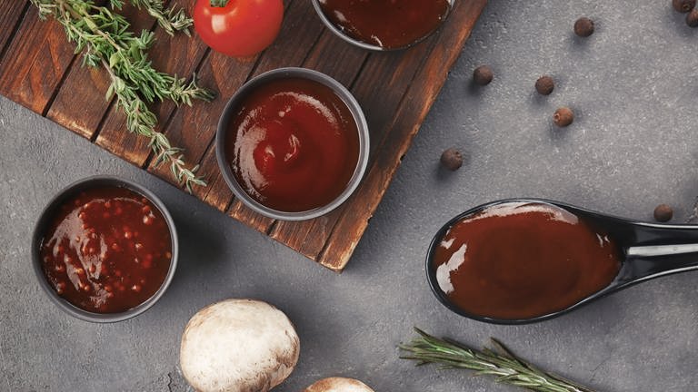 Auf einem Holzbrett mit Rosmarin, Tomate und Pilzen angerichtet: Dunkelrote süß-saure Soße. Marktcheck hat das Rezept. (Foto: Adobe Stock, Adobe Stock/Pixel-Shot)