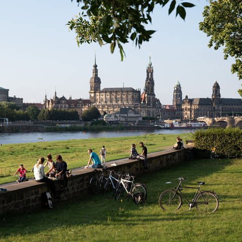 Das Bild zeigt das Elbufer, an einer Steinmauer stehen mehrere Fahrräder. Im Hintergrund auf der anderen Seite des Flusses ist eine alte Kathedrale zu sehen. (Foto: dpa Bildfunk, Picture Alliance)