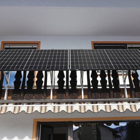 Zwei große Solarmodule sind am Geländer von einem Holzbalkon befestigt. Balkonkraftwerke von Lidl und Netto im Test (Foto: Colourbox)