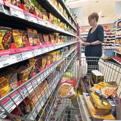 Frau mit Einkaufswagen im Supermarkt vor einem Regal mit Produkten von Maggi: Schnell und günstig kochen mit Fertigprodukten ist nicht unbedingt auch gesund (Foto: IMAGO, IMAGO / Martin Wagner)