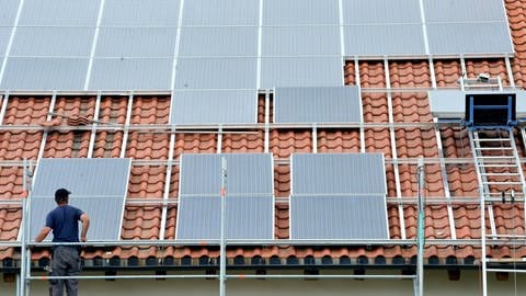 Solaranlage wird von einem Arbeiter auf einem Dach montiert. Mit einer Solaranlage lassen sich oft hohe Stromkosten vermeiden, denn aus Sonnenenergie wird Strom erzeugt. (Foto: dpa Bildfunk, picture alliance/dpa | Rolf Haid)