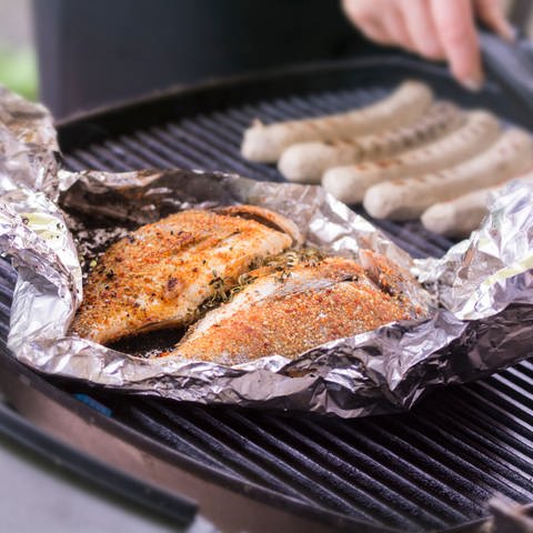 Fisch liegt in Alufolie auf einem Grill. Viele verwenden regelmäßig Alufolie, zum Beispiel zum Verpacken oder Abdecken von Essen und Lebensmitteln. Das ist nicht immer eine gute Idee - für die Gesundheit und die Umwelt. (Foto: IMAGO, 0135373407)