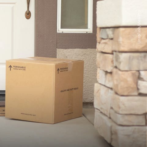 Ein großes, quadratisches Paket steht unbeaufsichtigt rechts vor einer Haustür. (Foto: Unsplash/MealPro)