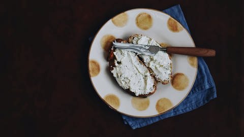 Ein Teller mit zwei geschmierten Scheiben Brot mit Frischkäse (Foto: Unsplash/Gaelle Marcel )