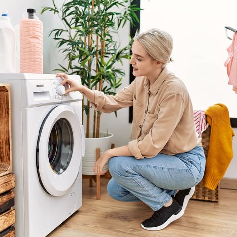 Blonde Frau hockt vor Waschmaschine und drückt einen Knopf. Trommelgröße: Wie verlässlich ist die Kilo-Angabe? (Foto: Adobe Stock)