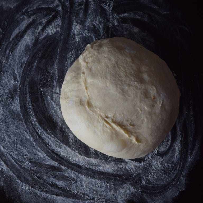 Roher Pizzateig auf schwarzem Hintergrund, Pizzateigrezept für zu Hause (Foto: Unsplash/Tamara Gak)