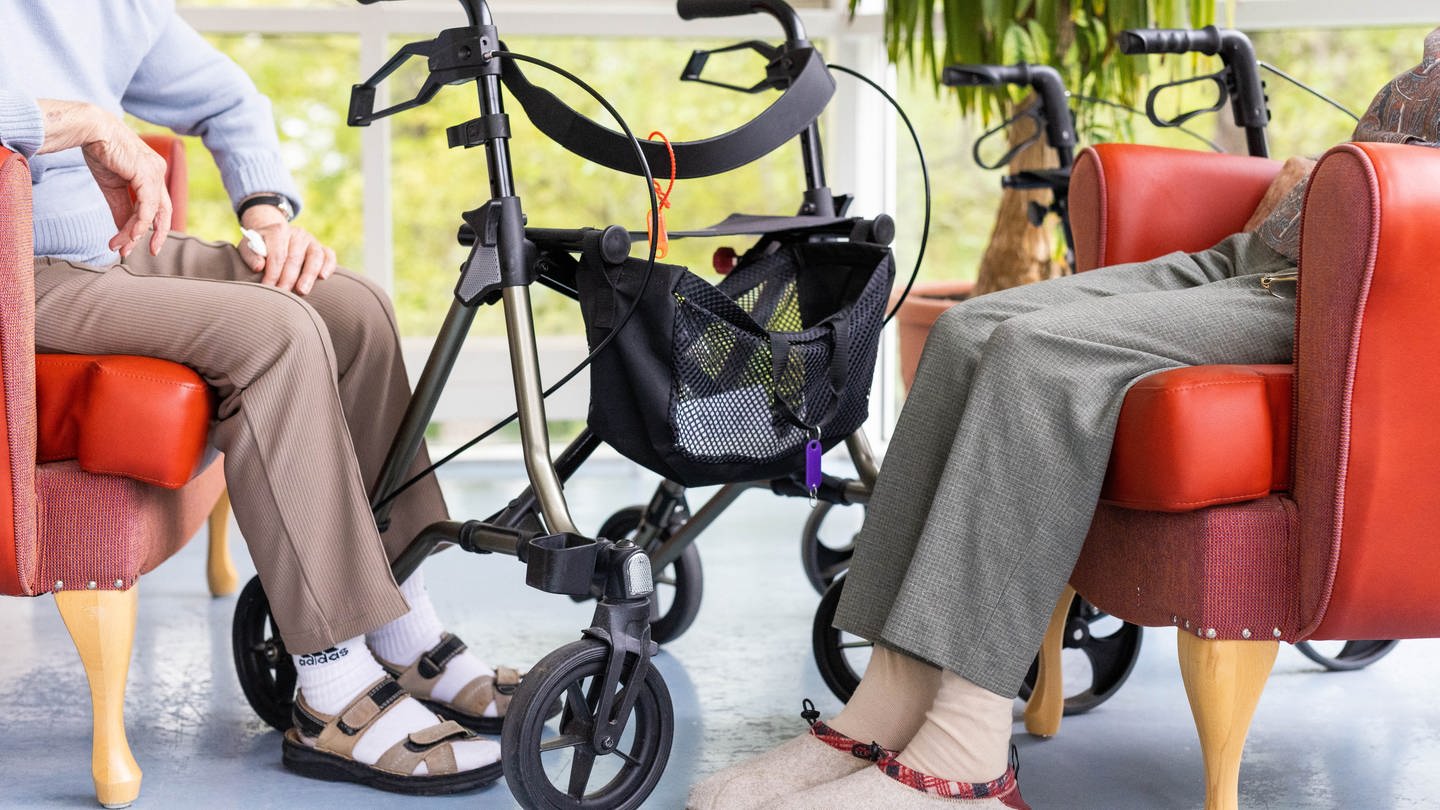 In einer Sitzgruppe in einem Pflegeheim sitzen zwei Senioren mit Rollatoren (Foto: dpa Bildfunk, Picture Alliance)
