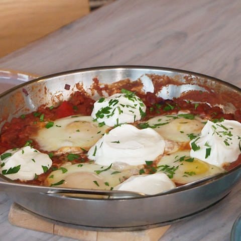Auf dem Tisch sind Teller und eine Pfanne mit Shakshuka. Shakshuka ist ein würziger Tomaten-Eintopf mit pochierten Eiern in der Pfanne, der traditionell zum Frühstück serviert wird. Das Gericht eignet sich aber auch als Mittag- und Abendessen.  (Foto: SWR)