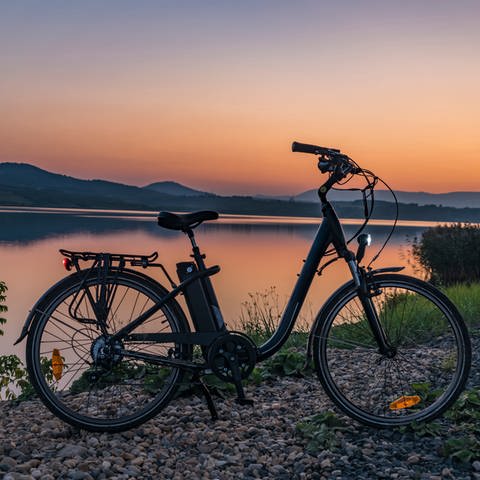 Ein E-Bike steht vor einem See bei Sonnenuntergang. Akkus: Brandgefahr und Entsorgung. (Foto: Adobe Stock, luzkovyvagon.cz)