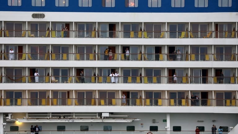 Passagiere stehen auf den Balkonen vom Kreuzfahrtschiff "Aidasol". Als erstes Kreuzfahrtschiff der Saison 2021 in Warnemünde läuft die "Aidasol" in den Seekanal ein.