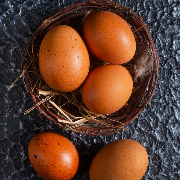 In einem Weidenkörbchen liegen drei braune Eier, davor liegen zwei weitere