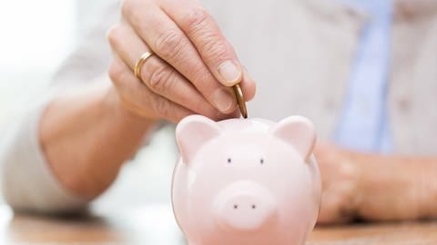 Seniorin wirft Geld in ihr Sparschwein. (Foto: Getty Images, Thinkstock - dolgachov)