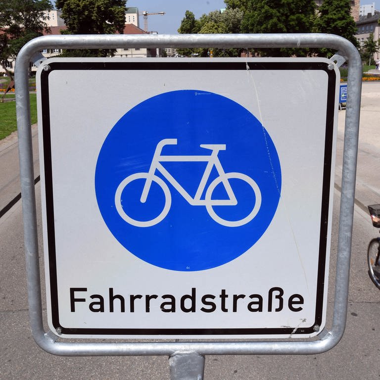 Auf einem blauen Schild mit weißem Hintergrund ist ein Fahrrad abgebildet. Darunter steht der Schriftzug Fahrradstraße. Neben dem Schild fährt eine Radfahrerin vorbei. (Foto: picture-alliance / Reportdienste, Uli Deck/dpa)