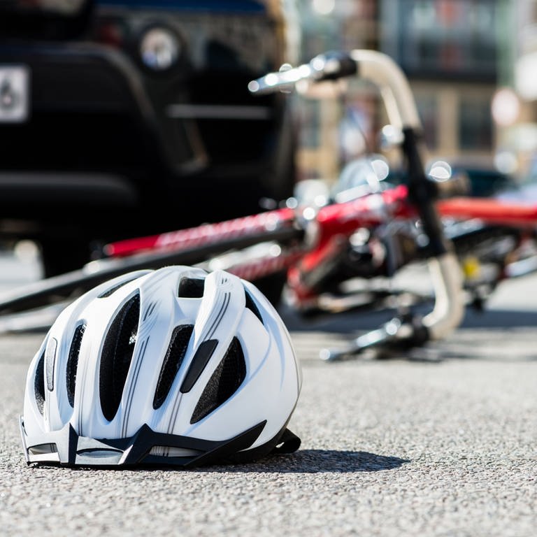 Fahrrad und Helm liegen nach einem Unfall mit einem Auto auf dem Straße. 
