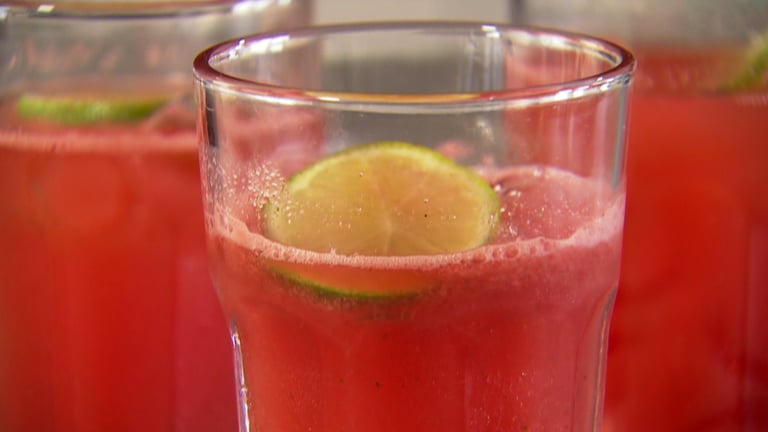 Hellrotes Getränk mit Limettenscheibe in Glas. Für dieses gesunde Smoothie Rezept braucht man Wassermelone, Apfelschorle, Zitrone oder Limette und Minze