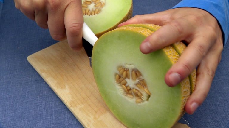Hand mit Messer schneidet innen grüne, außen blassgelbe Galiamelone auf. Alles Wissenswerte zu Honigmelonen, Zuckermelonen, Wassermelonen, Galia-, Netzmelone und Cantalup (Foto: SWR)