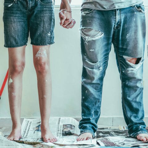 Zwei Leute stehen nebeneinander vor einer weißen Wand mit Farbpinseln in der Hand. Wie gesundheitsschädlich sind Wandfarben? Und welche Farbe passt am besten zur Einrichtung?