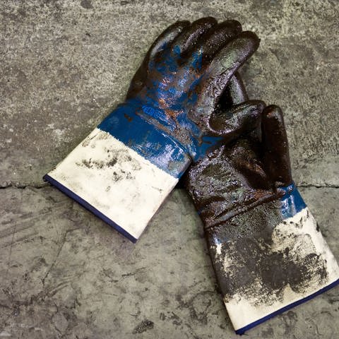 Schmutzige Handschuhe auf einem Boden. Sie sind mit Öl beschmiert.