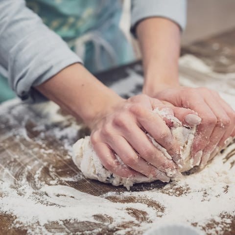 Zwei Hände kneten auf einer Arbeitsplatte Teig mit viel Mehl. Brotbackmischungen im Test: Welche Backmischung ist die beste?