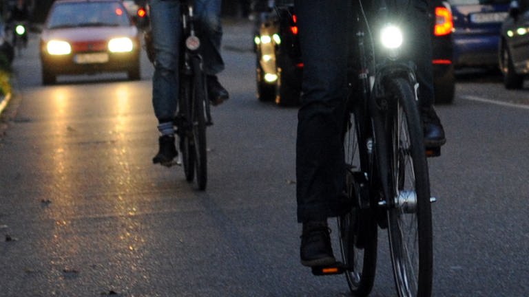 Ein Fahrrad mit Beleuchtung und eines ohne Licht fahren im Dunkeln nebeneinander (Foto: dpa Bildfunk, Picture Alliance)
