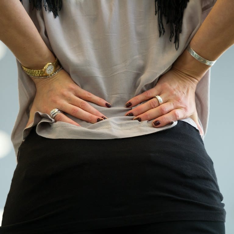 Frau von hinten, die die Hände in den Rücken stützt. Rückenschmerzen im unteren Rücken: Iliosakralgelenk, ISG, Bandscheibenvorfall? Welche Übungen helfen?